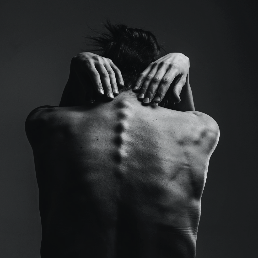 man sitting with hands grabbing toward his spine